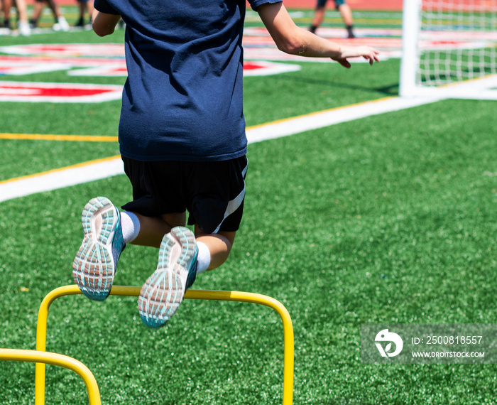 Kid jumping over yellow mini hurdle at camp