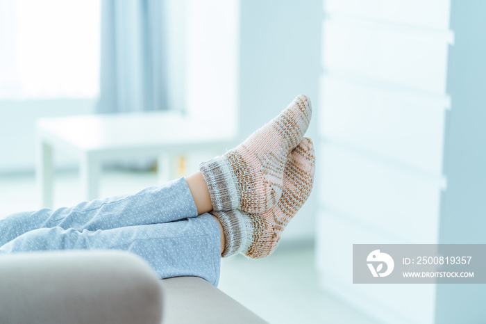 Woman resting on the sofa in pajamas and cozy soft comfortable knitted winter socks at home