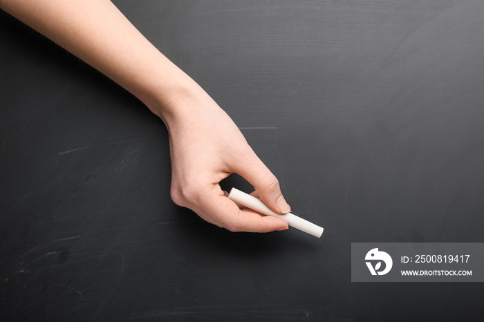 Female hand with piece of chalk on blackboard