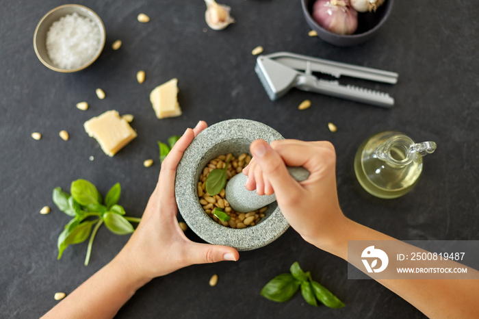 food cooking and culinary concept - hands grinding pine nuts in mortar and pestle for pesto sauce on stone table