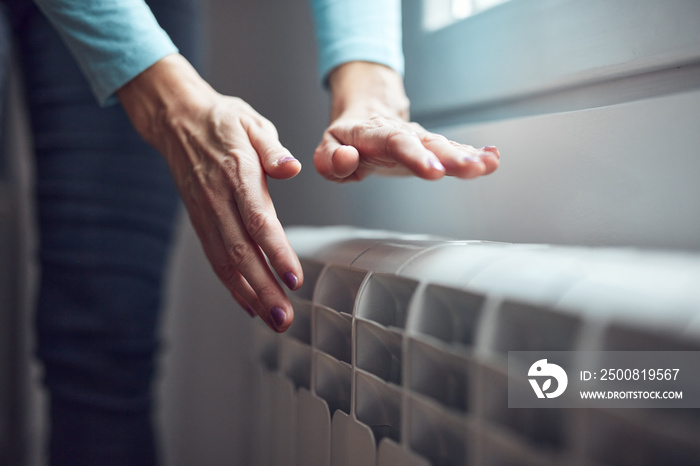 Woman heating her hands on the radiator during cold winter days.