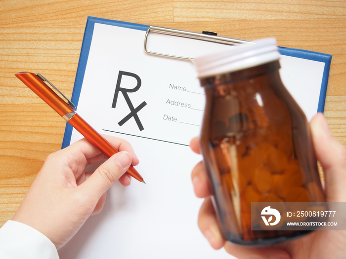 Female doctor hand holding blurred medical bottle and writing prescription form to patient at hospital or clinic. Pharmaceutical care, pain management and healthcare concept. Selective focus.