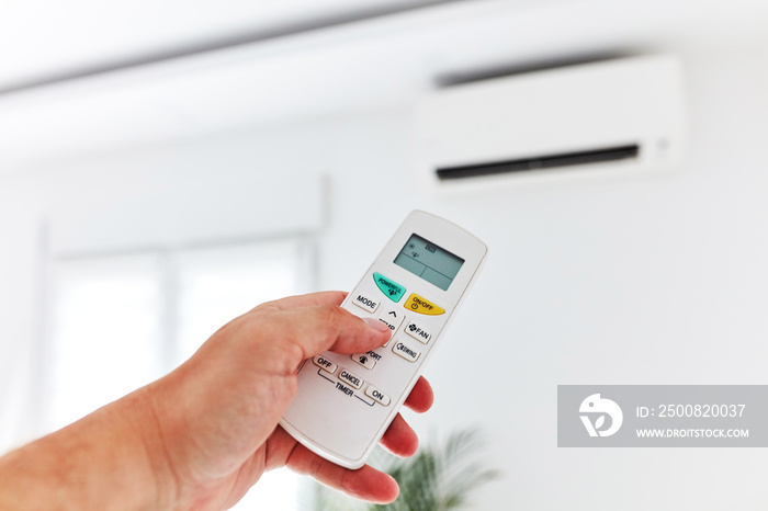 Modern air conditioner unit with a hand holding a remote.