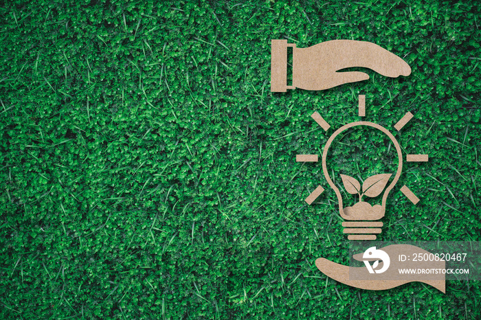 lightbulb with plant between hands paper cut on green grass background with copy space , green energy iconic symbol, save energy concept