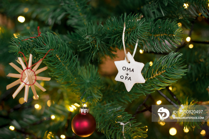 christbaumanhaenger selbstgemacht aus salzteig mit der aufschrift oma und opa im weihnachtsbaum haengend querformat