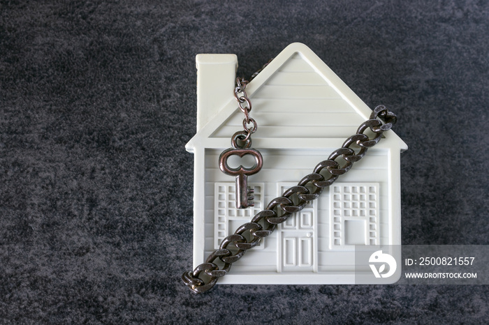 Small white house, chain and a decorative key on a dark background. Concept  -  risks, lose property,  seize, mortgage.