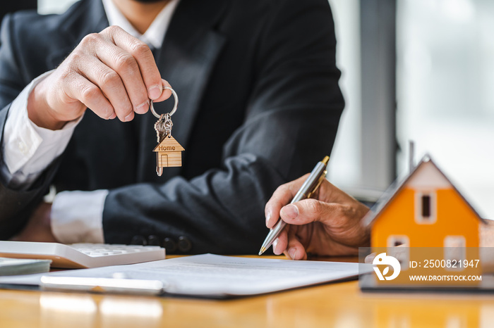 Real estate agent business man holding house key to his client after signing contract agreement in office,concept for real estate, moving home or renting property