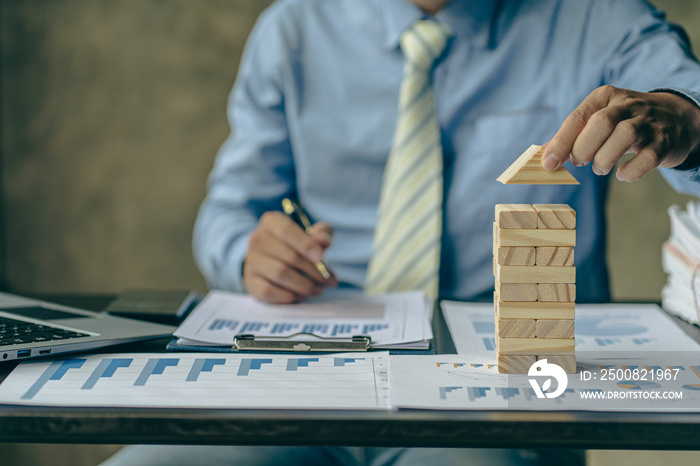 Businessman working with showing business graph Business expansion and growth plan With wooden block tower next to it with direction of growth and success, property and real estate insurance concept