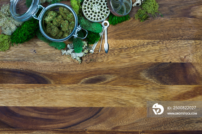 Marijuana in glass jar surrounded by moss, grinder, tool with wooden background