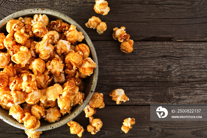 Bowl of caramel popcorn with scattered kernels. Close up top view over a rustic wood background with copy space