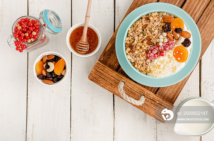 Healthy eating. Granola bowl with dried fruits, honey,milk, nuts and fresh red currant on white wooden background. Overhead, copy space