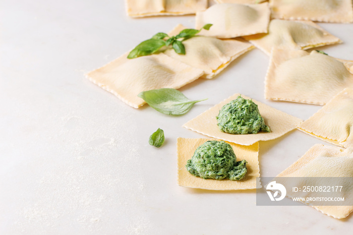 Homemade raw uncooked italian pasta ravioli staffed by spinach ricotta over white marble background. Close up, space