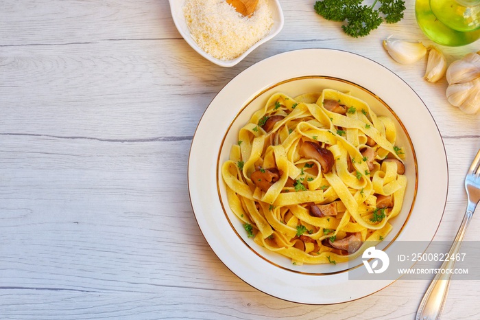 Italian Traditional Dish Tagliatelle ai funghi porcini ,tagliatelle pasta with porcini mushrooms,olive oil,garlics,parsley,salt and peppers on plate with white wood background.Top view.Copy space