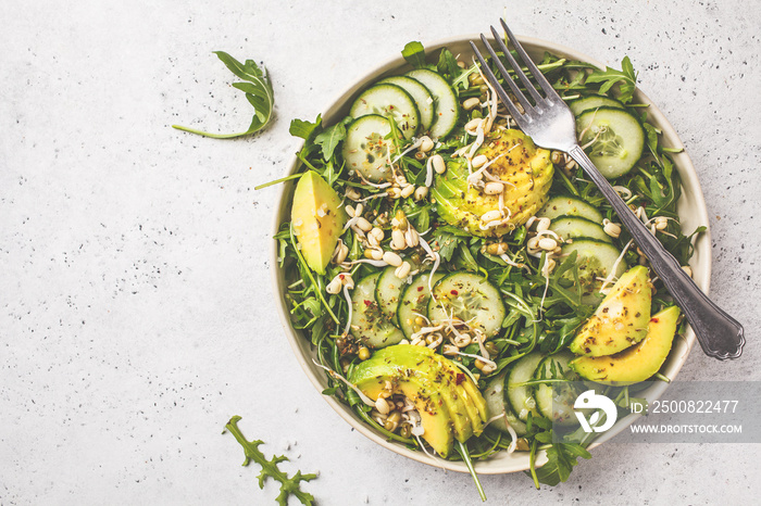 Healthy green salad with avocado, cucumber and arugula in white dish, top view, copy space.