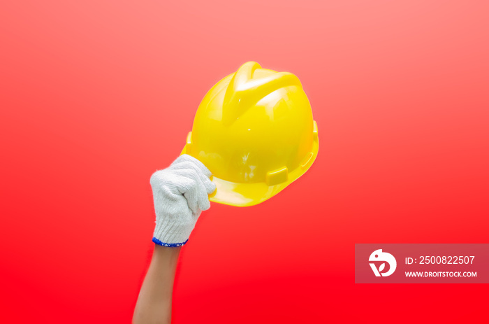 Male hand holding yellow safey hard hat isolated over red background. work safety concept. labour day concept.