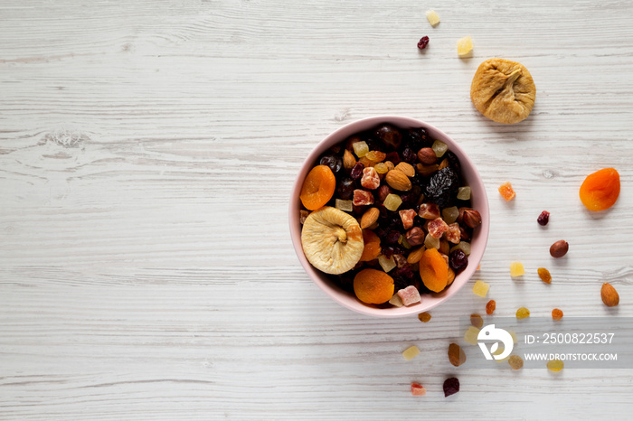 Dried fruits and nut mix in a pink bowl on white wooden background, top view. Overhead, from above, overhead. Copy space.