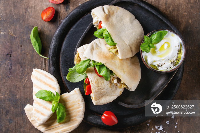 Pita bread sandwiches with grilled vegetables paprika, eggplant, tomato, basil and feta cheese served on black chopping board over dark wooden background. Healthy fast food concept. Top view space