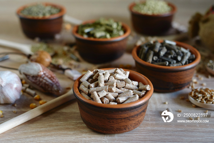 Different kinds of pelleted compound feed in bowls and spoons on wood table, copy space