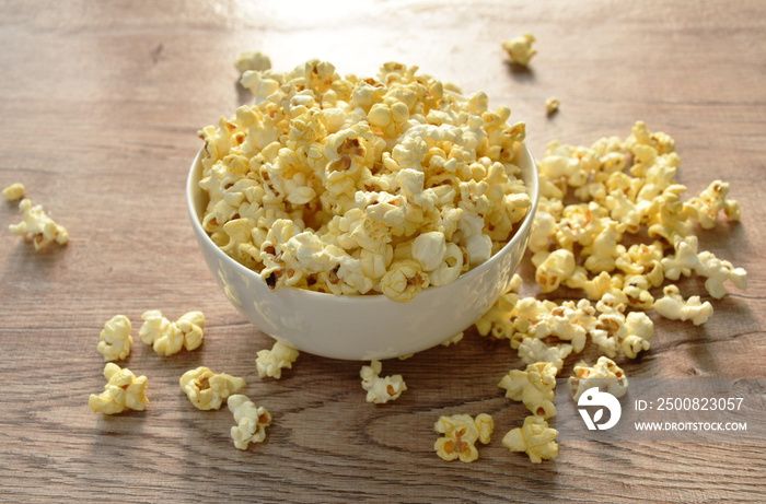 salty popcorn spreading  from bowl on wooden table