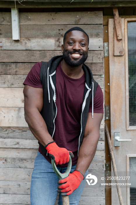 Portrait of smiling man standing in front of hut in urban garden