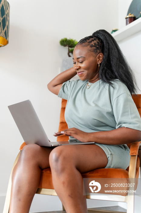 Young woman using laptop while sitting in armchair at home