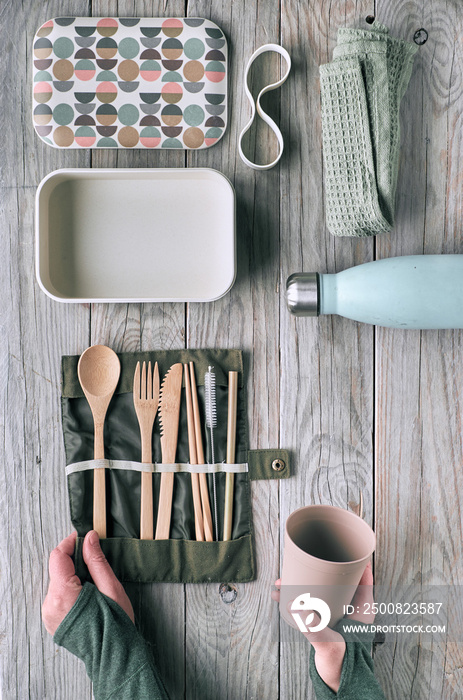 Creative flat lay, zero waste lunch concept with set of reusable wooden cutlery, lunch box, drinking bottle and reusable coffee cup. Sustainable lifestyle top view, flat layout on aged wood.