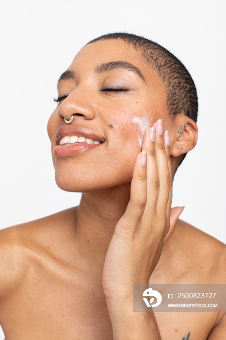 Studio portrait of woman applying face cream on cheek with eyes closed