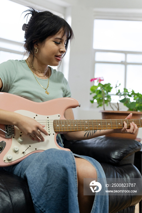 Young woman sitting on sofa and playing guitar