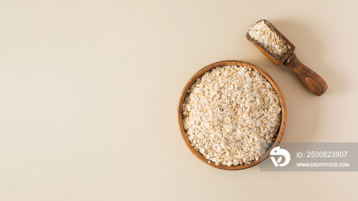 Oat flakes in a wooden bowl on a beige background. Healthy eating.