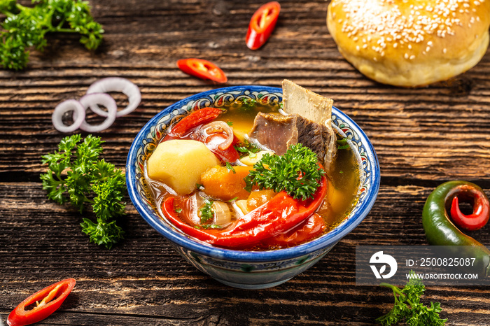 Soup Uzbek shurpa with beef and vegetables, in plate with oriental ornament, wooden background, concept of oriental Uzbek cuisine