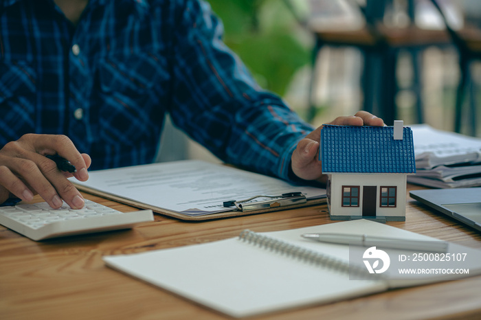 Real estate office, home sales agent sitting at desk with contract documents and house plans next to sale and rental concept.