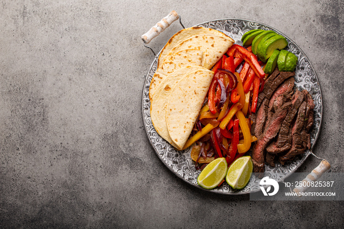 Traditional Mexican dish Beef fajita served with tortillas and ripe avocado on rustic metal plate and stone background from above, American Mexican food healthy meal with space for text