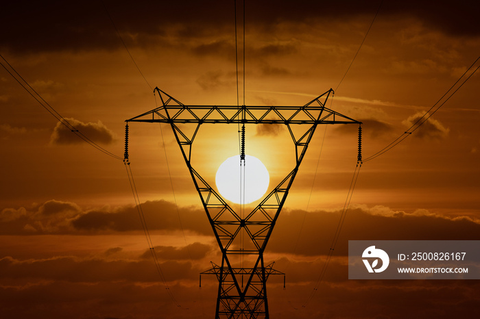 Energy Crisis. Electricity Pylon silhouetted at sunset. Electricity pylon or tower framing the setting sun. Symbolic with fossil fuels pylons and wires criss cross the country