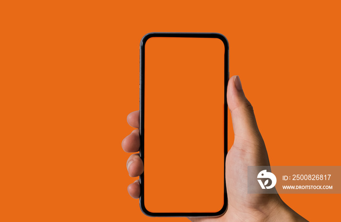 Hand holding white mobile phone with blank orange screen in orange background.