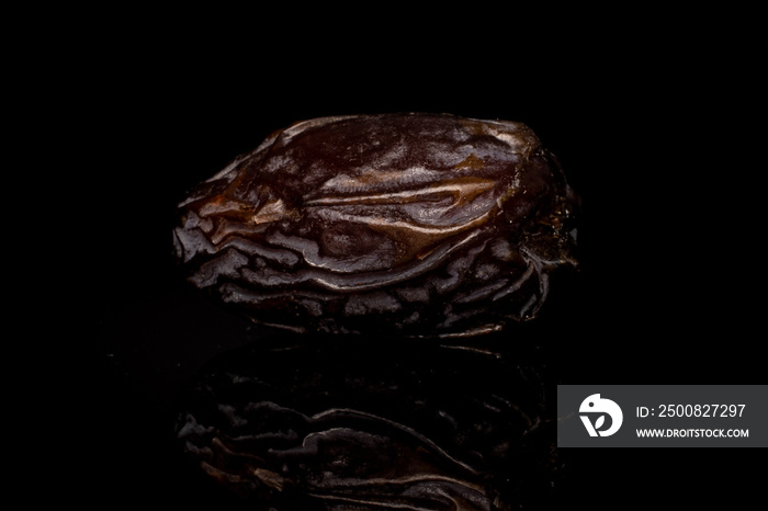 One whole dried brown date fruit isolated on black glass