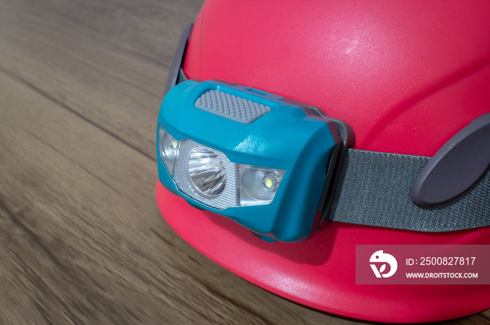 Teal led headlamp turned off strapped to a pink climbing helmet on a wooden table