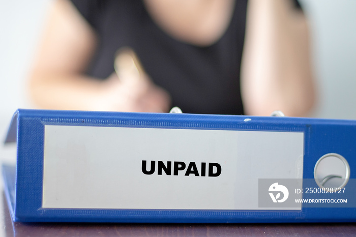 Folder labelled with the word unpaid in front of a woman sitting behind her office desk