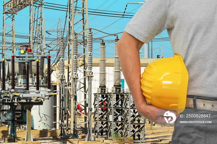 Hand of worker with yellow hard hat on high voltage power transformer substation background. Electrician Industry workers. Electric current redistribution substation