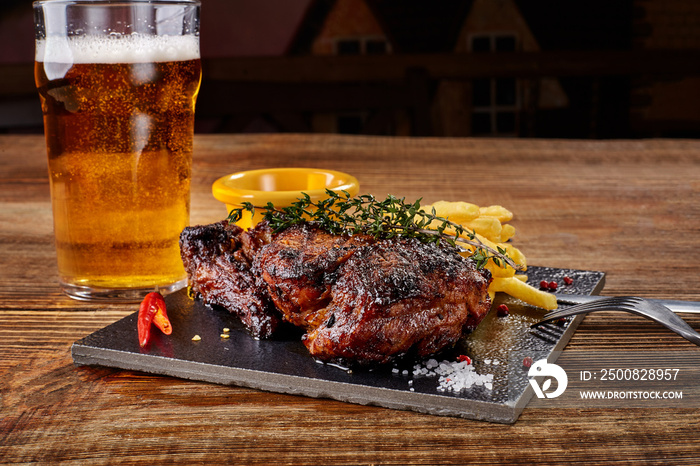 Beer being poured into glass with gourmet steak and french fries on wooden background.