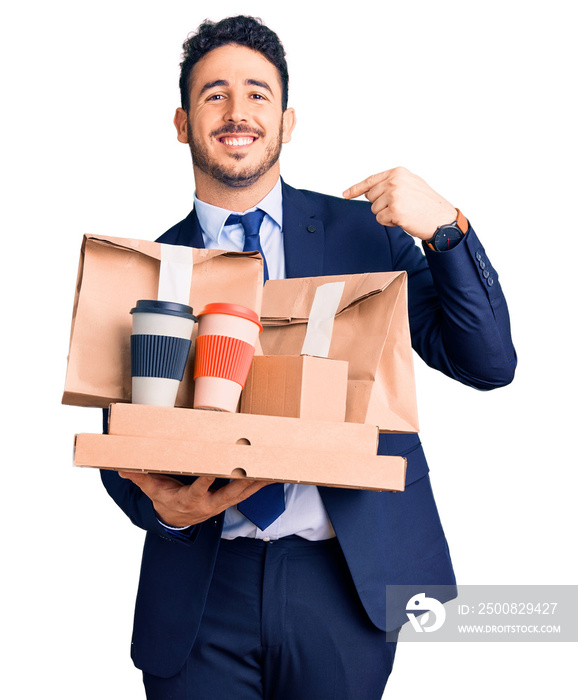 Young hispanic man wearing suit holding takeaway coffee and food pointing finger to one self smiling happy and proud