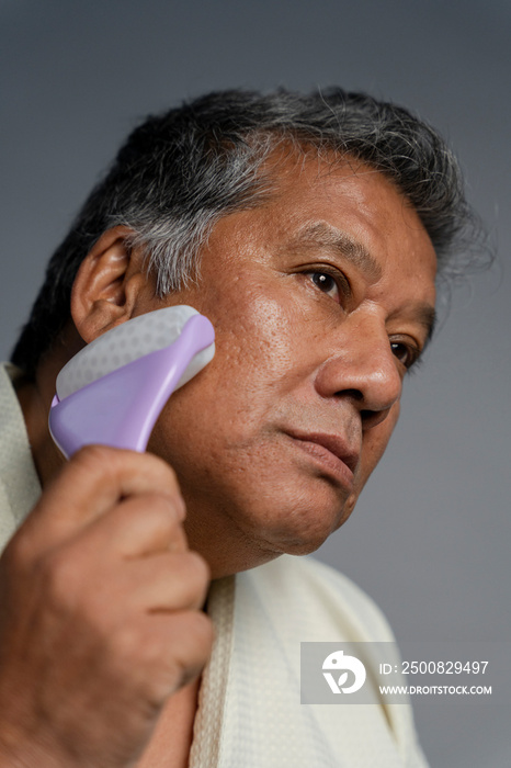 Portrait of serious man doing face massage with roller