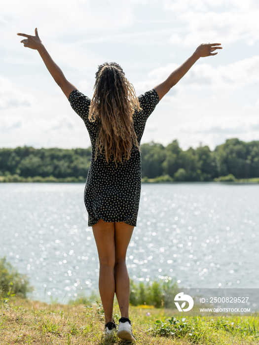 Woman standing with arms outstretched by lake on sunny day