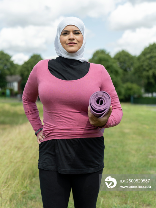 UK,Sutton,Portrait of woman in headscarf standing in meadow with yoga mat