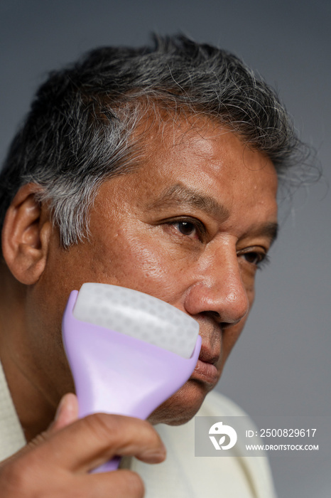 Portrait of serious man doing face massage with roller