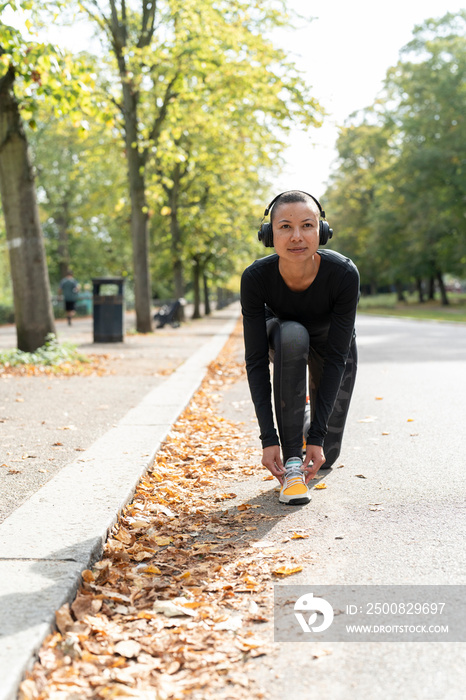 Portrait of woman in sports clothing and headphones tying shoe in park