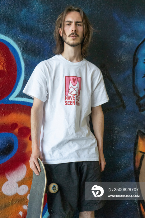 Portrait of young man standing against graffiti wall and holding skateboard