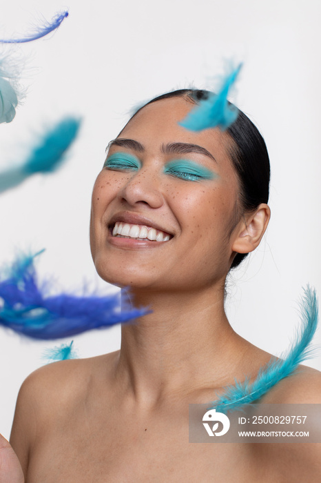 Blue feathers falling in front of smiling woman with closed eyes