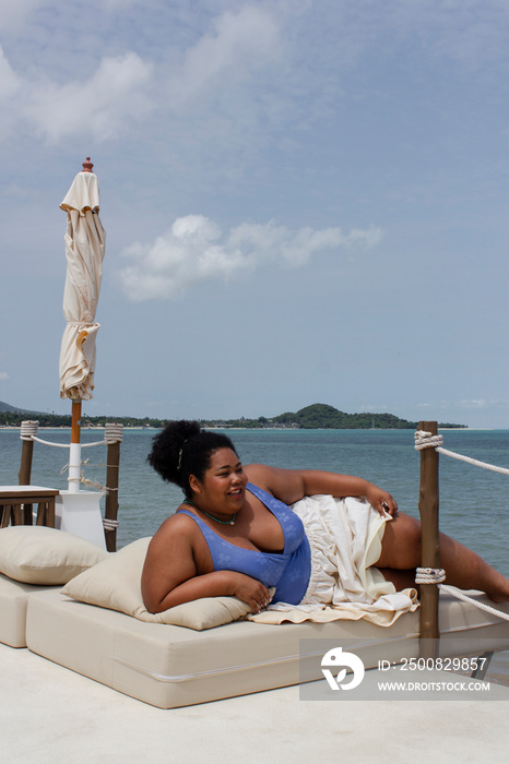 Young woman relaxing on sun lounger near bay