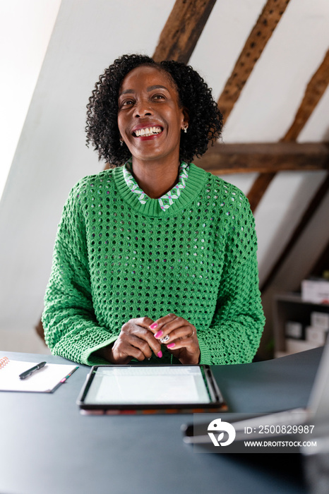 Smiling businesswoman working on digital tablet by desk in office