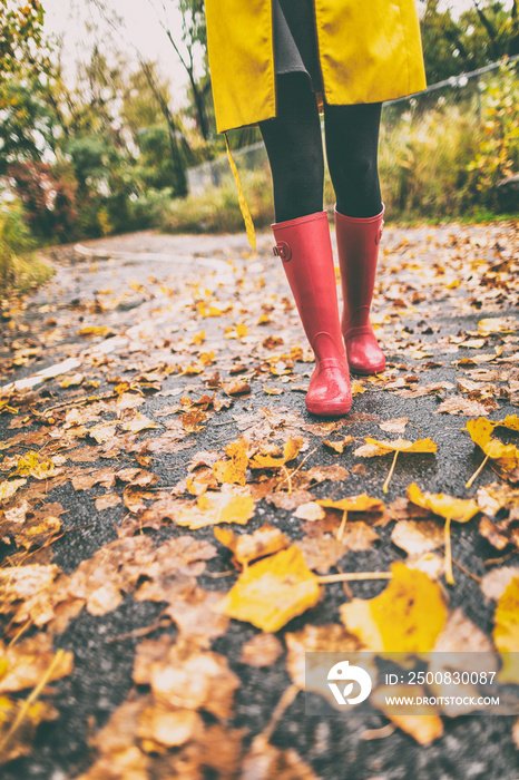 Red rubber boots woman walking in autumn leaves street in park. Fall fashion lifestyle.